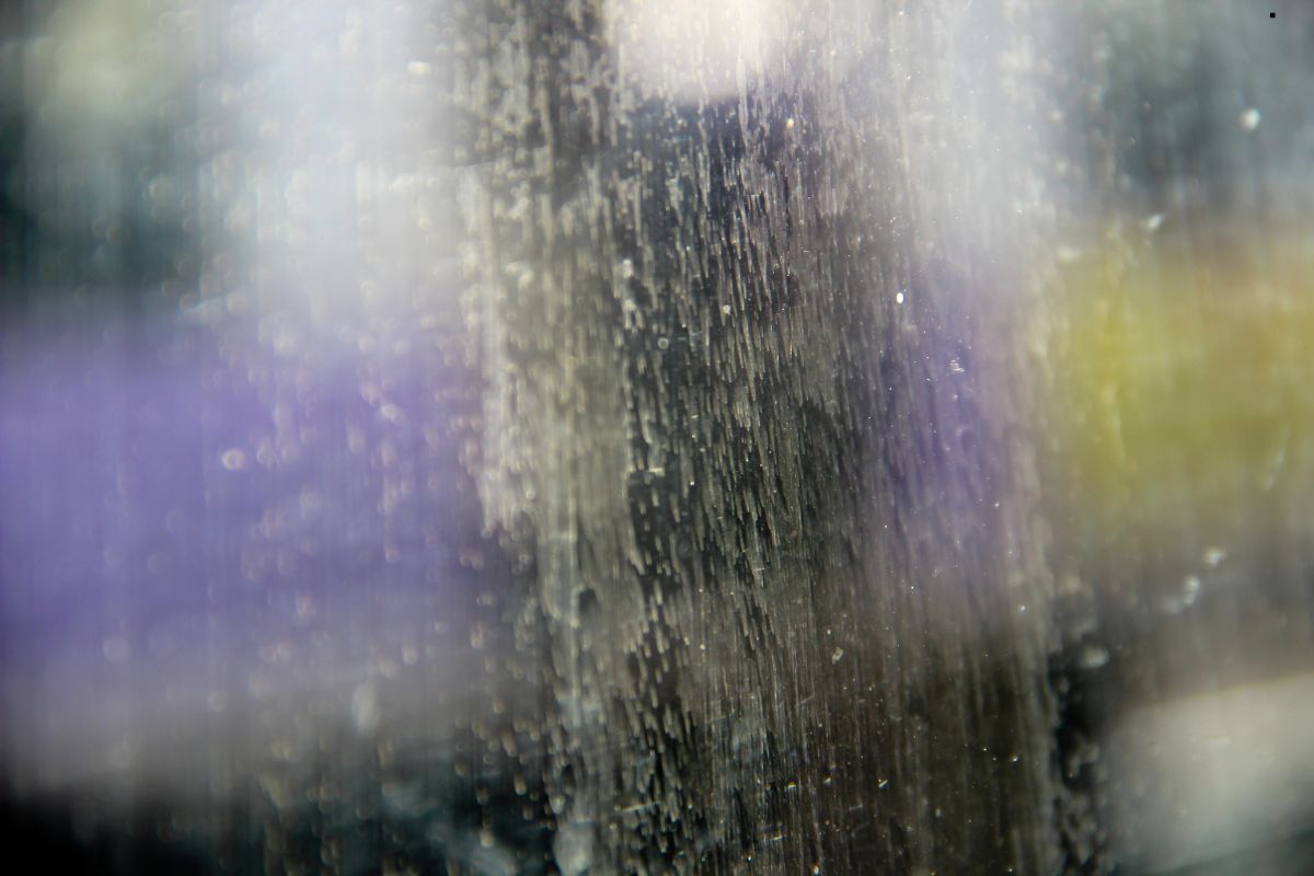 A close-up of a water droplet on a window, highlighting stubborn stains in the background.