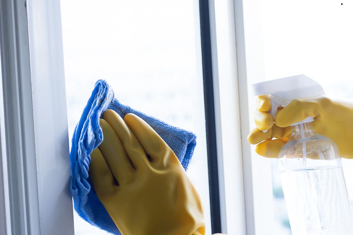 An individual in rubber gloves meticulously cleans a window with specialized tools for effective window maintenance.