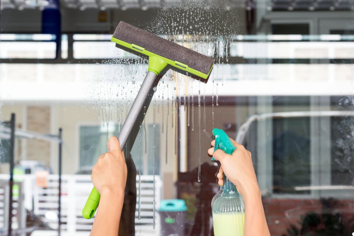 A person using a green brush to clean a window, focusing on removing dirt and smudges for a clear view.