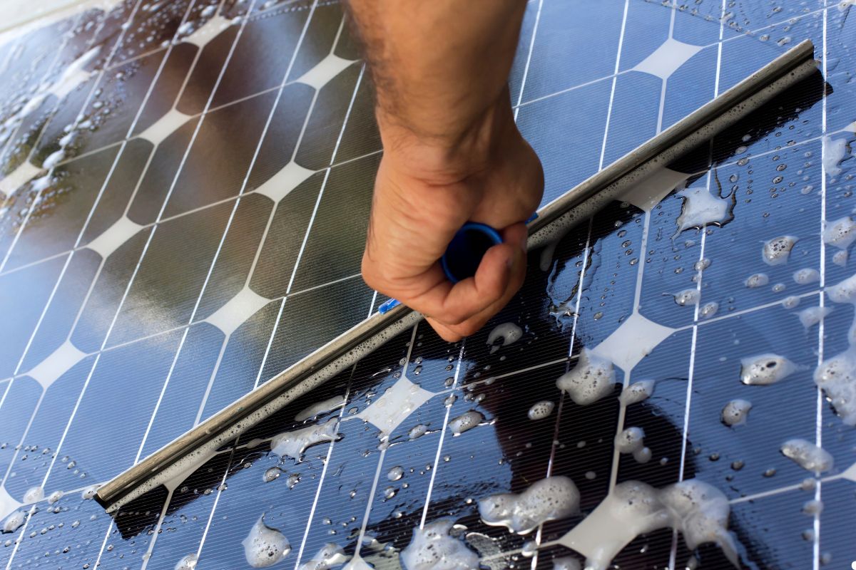 A person using a brush to clean a solar panel, ensuring optimal performance and efficiency. 