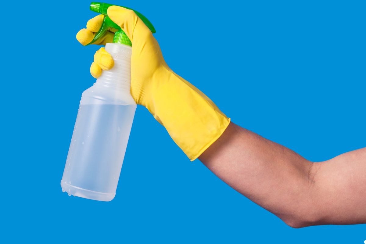 A person in yellow gloves holds a spray bottle, ready to clean or apply a solution.