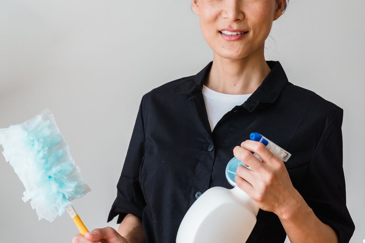 A woman wearing a black shirt holds a cleaning product, ready to clean her surroundings with a focused expression. 
