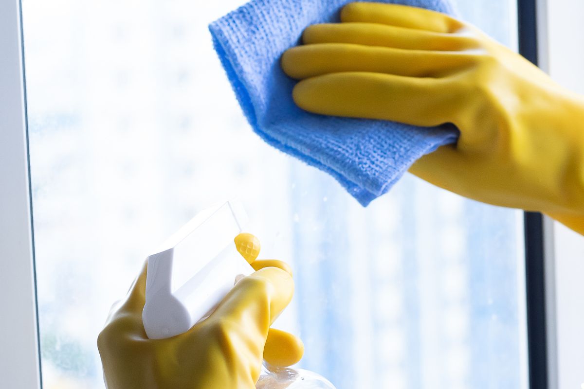 A person wearing yellow rubber gloves cleans a window with a cloth, focusing on removing dirt and smudges.